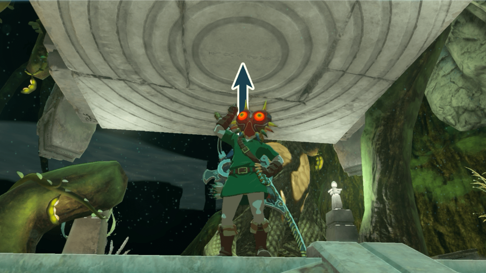 Link wearing Majora’s Mask hat pointing towards a large stone pillar with a ringed pattern on it in the Depths in The Legend of Zelda: Tears of the Kingdom.