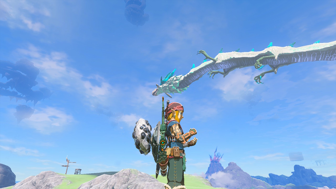 Naydra the dragon flies through the sky while Link stands on the ground during a sunny day in Zelda Tears of the Kingdom.