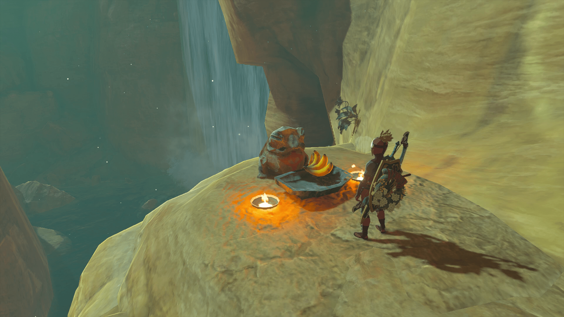Link stands in front of a frog with a Yiga Clan symbol on it in Tears of the Kingdom. There are two torches by the frog with a banana offered in front.